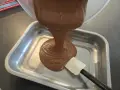 Comment faire une ganache : du chocolat fondu coule d'un bol dans un plat, guidé par une spatule.