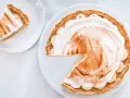Une part de tarte banoffee traditionnel, garnie de crème fouettée et de cannelle, sur une assiette blanche.