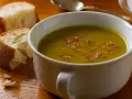 Un bol de soupe de pois cassés fumante, garnie de lardons, avec du pain croustillant à côté. Un délice réconfortant.