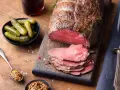 Un délicieux roti de boeuf, tranché et servi avec des cornichons, de la moutarde et une boisson foncée.
