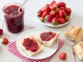 Un pot de confiture de fraise maison, des tartines de pain frais garnies de cette confiture, et des fraises fraîches. Un délice !