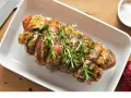 Rôti de porc Orloff, assaisonné et garni de romarin frais, prêt à être cuit dans un plat blanc.
