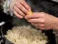 Des mains pressent un citron sur une soupe de riz fumante, ajoutant une touche de fraîcheur à ce plat réconfortant.