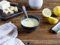 Un bol de sauce beurre citron, avec des citrons, du beurre coupé en dés et une râpe à zester sur une table en bois.