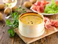 Un délicieux Mont d'Or crémeux, prêt à être dégusté avec du jambon cru, des pommes de terre et un verre de vin blanc.