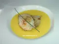 Deux filets de poisson poêlés reposent dans une onctueuse sauce à l'orange, décorés d'une tige de ciboulette.