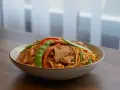 Un plat de nouilles asiatiques avec de l'émincé de porc, des pois gourmands et des poivrons rouges.