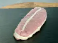 Rôti de veau cru ficelé, prêt à cuire, sur une planche sombre.