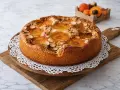 Un délicieux gâteau aux abricots, garni d'amandes effilées, est présenté sur une planche en bois.