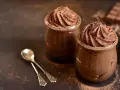 Deux pots de mousse au chocolat onctueuse, saupoudrés de cacao, avec deux cuillères argentées.