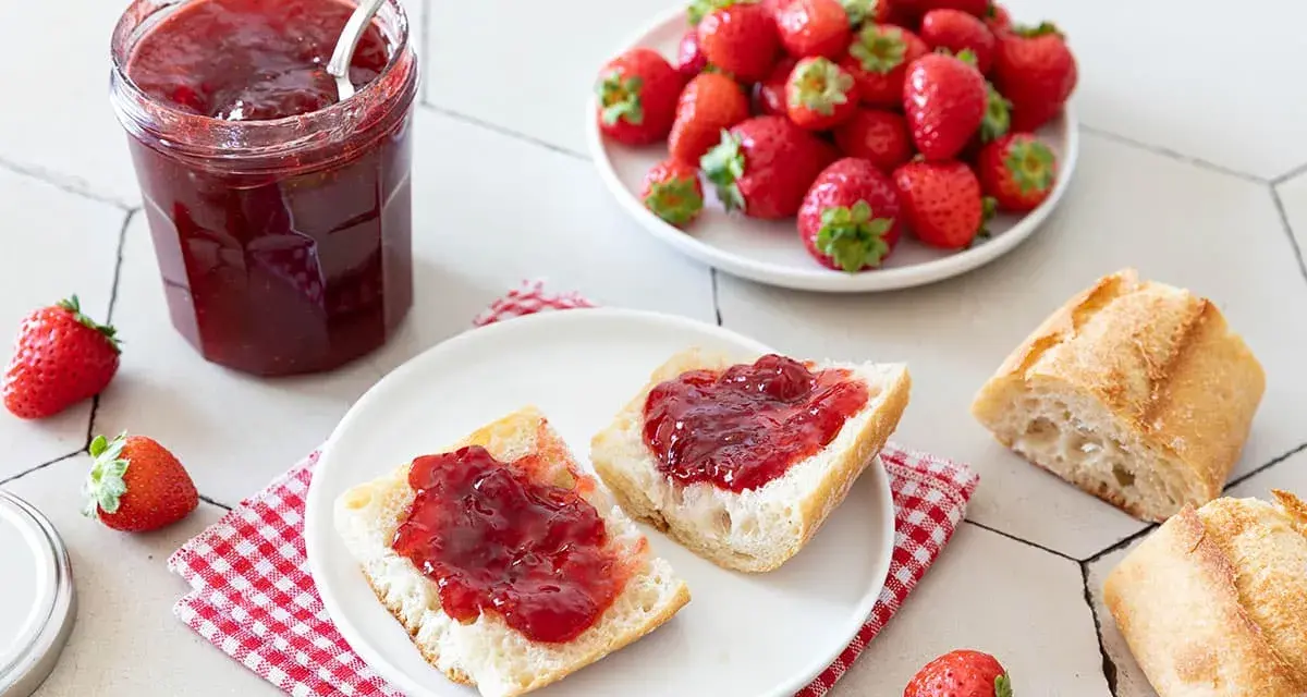 Un pot de confiture de fraise maison, des tartines de pain frais garnies de cette confiture, et des fraises fraîches. Un délice !