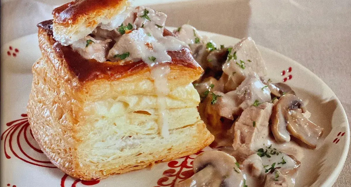 Une bouchée à la reine au veau, garnie de morceaux de veau et de champignons dans une sauce crémeuse, servie sur une assiette décorée.