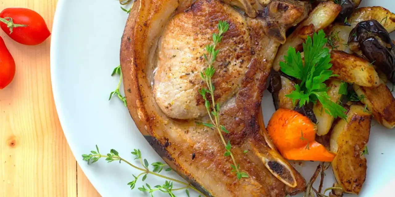 Une côte de porc savoureuse accompagnée de légumes rôtis, de pommes de terre et de tomates cerises.