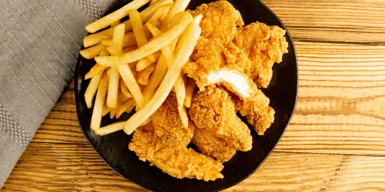 Assiette de nuggets maison dorés et croustillants avec des frites, sur fond de bois.