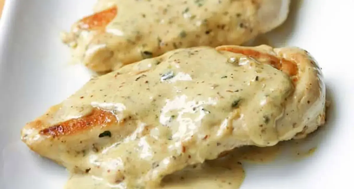 Deux morceaux de poulet à la crème, nappés d'une sauce onctueuse aux herbes, sur une assiette blanche.
