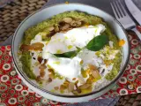Un bol de purée verte, peut-être une sauce petit pois, garni d'un œuf poché, de crème, d'amandes effilées et d'une feuille de basilic.
