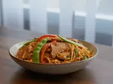 Un plat de nouilles asiatiques avec de l'émincé de porc, des pois gourmands et des poivrons rouges.