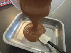 Comment faire une ganache : du chocolat fondu coule d'un bol dans un plat, guidé par une spatule.