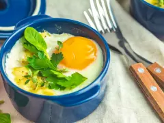 Un œuf cocotte appétissant dans un ramequin bleu, garni d'herbes fraîches. Un délice pour le petit-déjeuner.