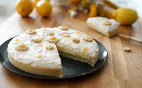 Tarte au citron décorée de petites fleurs en biscuit. Une part est coupée, révélant la crème pâtissière. Parfait pour une recette de tarte.