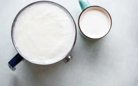 Un pot de lait chaud avec une fine peau de lait à la surface, à côté d'une tasse remplie de lait frais.