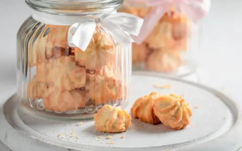 Biscuits sablés dans des bocaux en verre décorés de rubans blancs et roses, parfaits pour un dessert pique-nique.