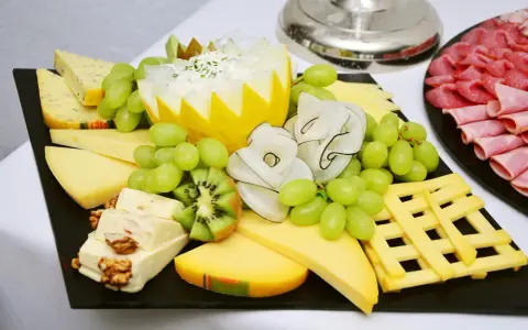 Plateau de fromage festif avec raisins verts, kiwi, noix et charcuterie. Une belle décoration plateau de fromage pour un événement.