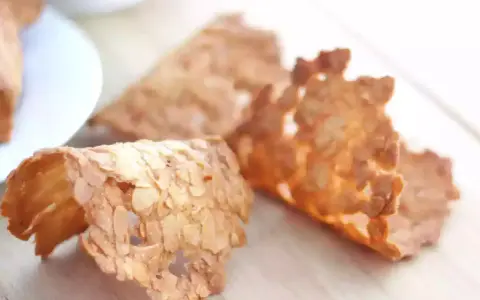 Trois tuiles aux amandes croustillantes, dorées et délicates, posées sur une planche en bois.
