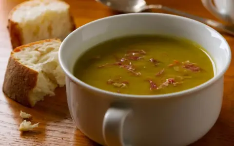 Un bol de soupe de pois cassés fumante, garnie de lardons, avec du pain croustillant à côté. Un délice réconfortant.