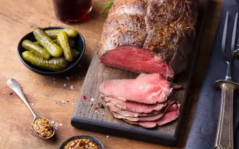 Un délicieux roti de boeuf, tranché et servi avec des cornichons, de la moutarde et une boisson foncée.