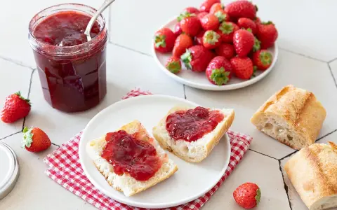 Un pot de confiture de fraise maison, des tartines de pain frais garnies de cette confiture, et des fraises fraîches. Un délice !