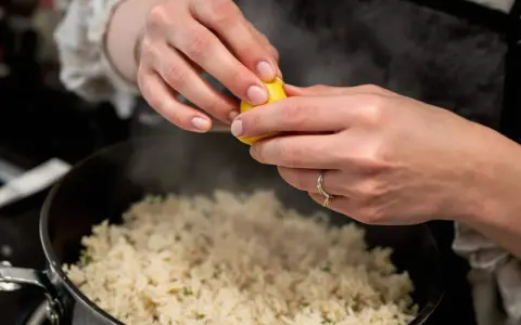 Des mains pressent un citron sur une soupe de riz fumante, ajoutant une touche de fraîcheur à ce plat réconfortant.