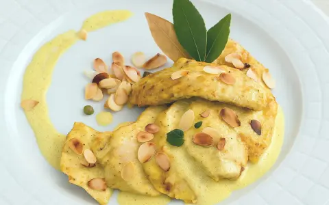 Délicieux poulet au curry, garni d'amandes effilées et d'une sauce onctueuse, servi sur une assiette blanche.
