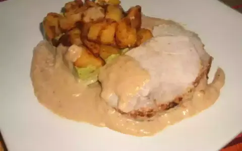 Tranche de roti de porc au lait, nappée d'une sauce onctueuse, accompagnée de pommes de terre rôties croustillantes. Un plat réconfortant.