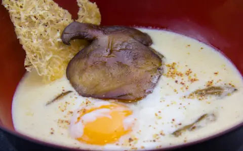Un œuf parfait, crémeux et onctueux, baigne dans une soupe onctueuse, garnie d'un champignon poêlé et d'une tuile croustillante.