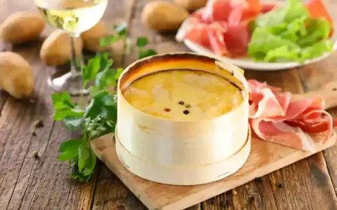 Un délicieux Mont d'Or crémeux, prêt à être dégusté avec du jambon cru, des pommes de terre et un verre de vin blanc.