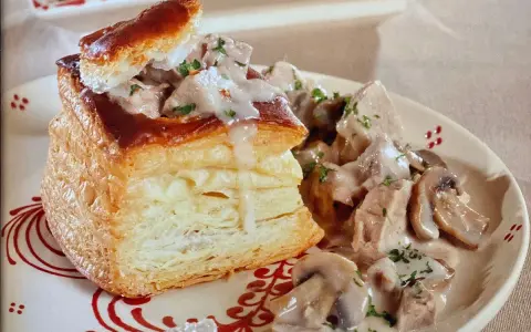 Une bouchée à la reine au veau, garnie de morceaux de veau et de champignons dans une sauce crémeuse, servie sur une assiette décorée.