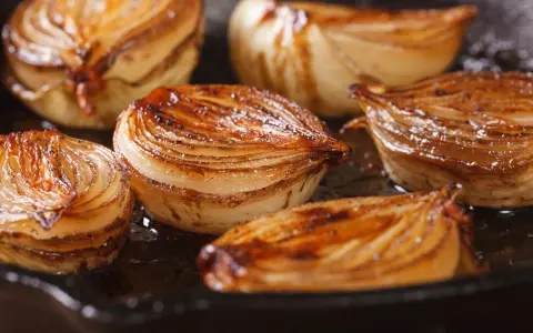 Moitiés d'oignons caramélisés, dorés et juteux, cuisant dans une poêle.
