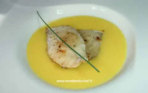 Deux filets de poisson poêlés reposent dans une onctueuse sauce à l'orange, décorés d'une tige de ciboulette.
