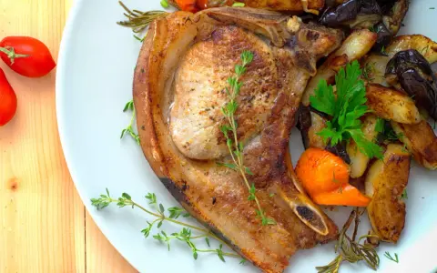 Une côte de porc savoureuse accompagnée de légumes rôtis, de pommes de terre et de tomates cerises.