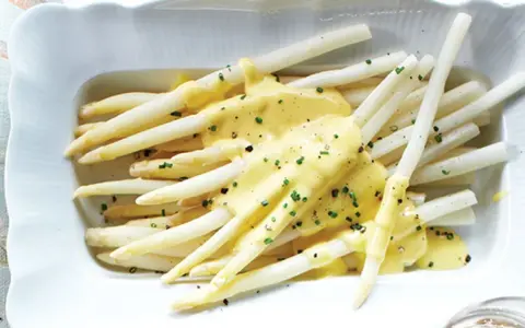 Asperges blanches nappées d'une sauce onctueuse, parsemées de ciboulette fraîche. Un délice printanier.