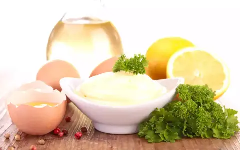 Un bol de mayonnaise maison crémeuse, entouré d'œufs, de citron, d'huile et de persil.