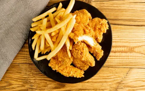Assiette de nuggets maison dorés et croustillants avec des frites, sur fond de bois.