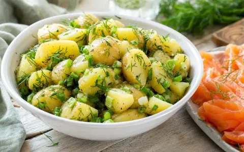 Salade de pommes de terre fraîchement préparée, garnie d'aneth et de ciboule, prête à être servie avec une sauce légère.