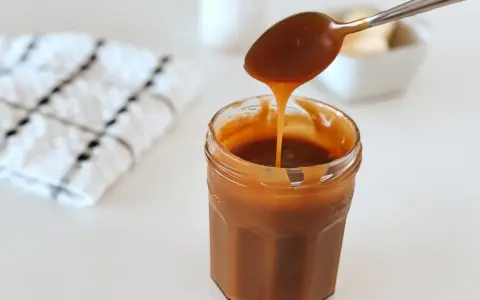 Une cuillère verse du caramel onctueux dans un pot. La recette caramel parfaite pour vos desserts.