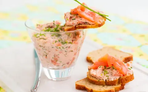 Rillettes de saumon crémeuses dans un verre, garnies de fines herbes et servies sur des toasts avec des tranches de saumon fumé.