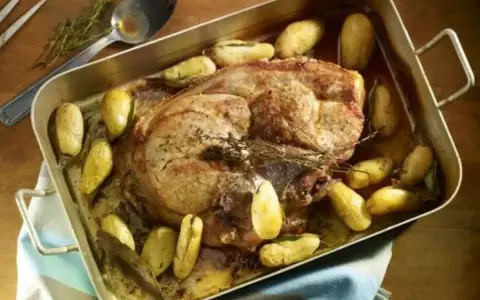 Rouelle de porc rôtie au four, entourée de pommes de terre dorées et d'herbes aromatiques. Un plat savoureux prêt à être dégusté.