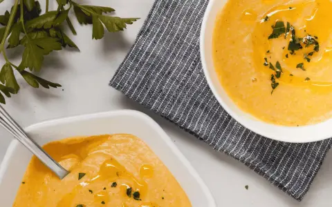 Deux bols de velouté de butternut facile, ornés d'huile d'olive et de persil frais, prêts à être dégustés.