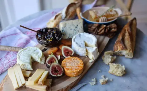 Plateau de fromages variés, dont un fromage à pâte cuite, avec figues, confiture et pain.