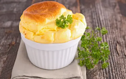 Un soufflé au fromage doré et gonflé, garni de persil frais, dans un ramequin blanc sur une serviette grise.